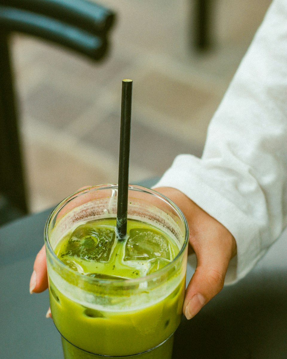 A hand holding a glass of iced matcha latte